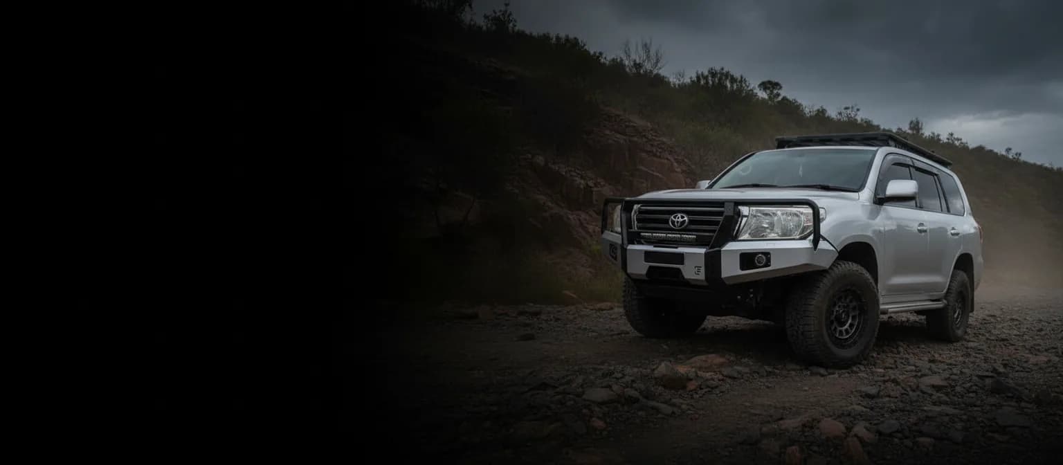A lifted white LandCruiser with a steel bull bar on a rocky Queensland track under a storm sky