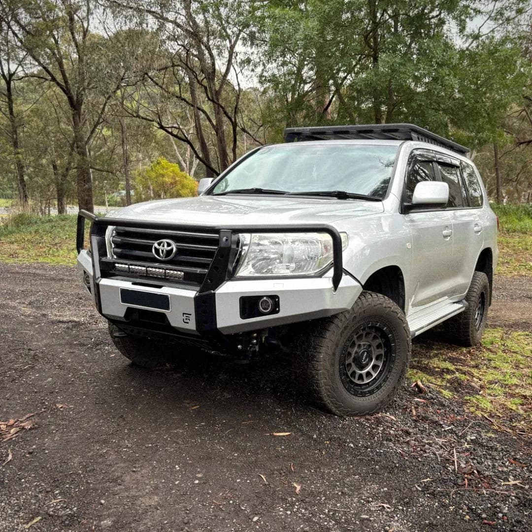 A 200 Series LandCruiser with a bull bar and roof rack on a bush track