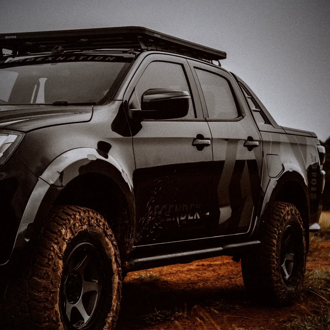 A dark grey D-Max with a roof rack and a Legendex door decal on red dirt