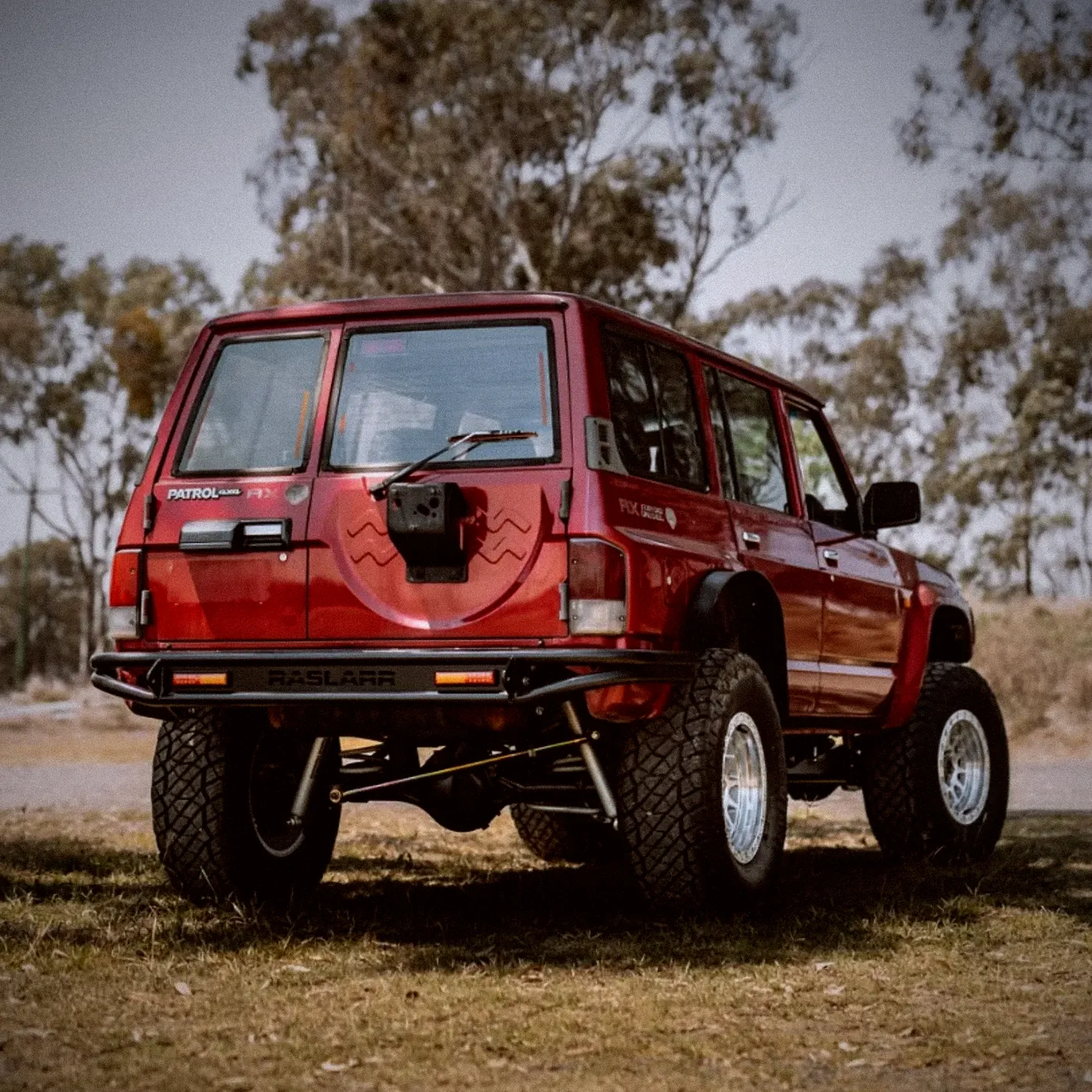 A lifted red GQ Patrol from behind, with a Raslarr rear bar, on grass under gum trees